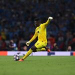 André Onana in Manchester United kit during a match, with Bayer Leverkusen and UEFA Champions League logos in the background, symbolizing his €20 million transfer and reunion with coach Erik ten Hag.