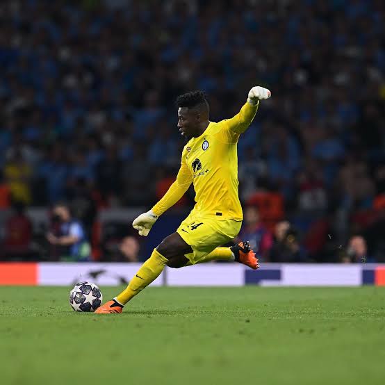 André Onana in Manchester United kit during a match, with Bayer Leverkusen and UEFA Champions League logos in the background, symbolizing his €20 million transfer and reunion with coach Erik ten Hag.
